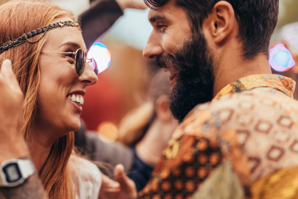 Een man en een vrouw in hippie-achtige kleding kijken elkaar aan terwijl ze dansen op een festival