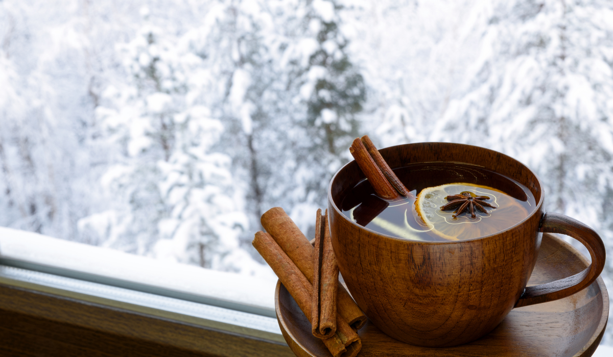 Foto van een kopje thee naast een raam. Buiten sneeuwt het.