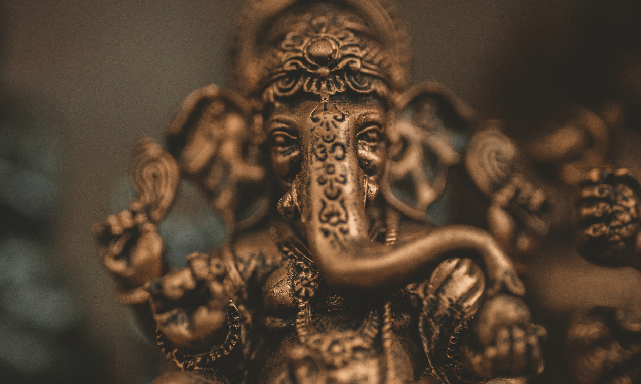 Een foto van een bronzen beeld van Ganesha, tegen een neutrale achtergrond.