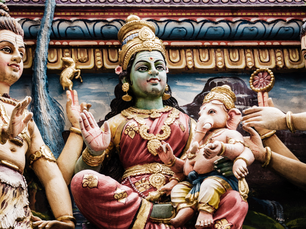 Een kleurrijk standbeeld van meerdere Deva's uit het Hindoeïsme. In het midden zit Parvati met een kleine Ganesha op haar knie