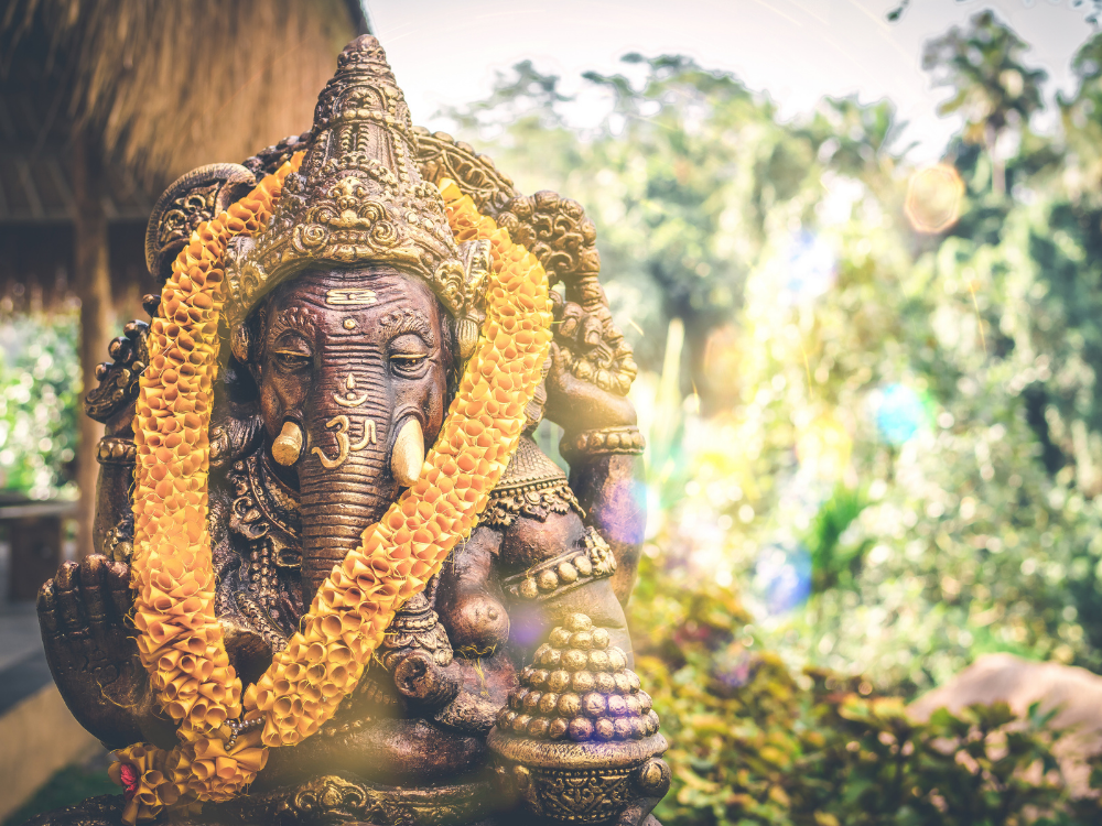 Een groot beeld van Ganesha waar een bloemenkrans omheen is gelegd. Het beeld lijkt in een oerwoud te staan