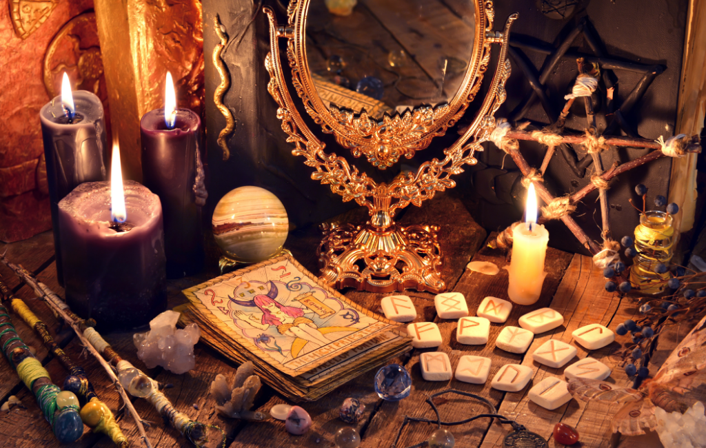 Een tafel vol met wicca-gerelateerde spullen, zoals een kaartendeck, setje runenstenen, kaarsje, edelstenen, spiegel, kruiden en nog veel meer